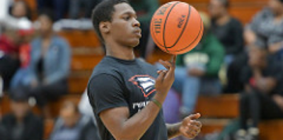 A basketball player spins the ball on the tip of one finger while the audience in the bleachers looks on